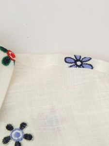 Détail de la broderie florale sur chemise en lin beige avec motifs de fleurs colorés