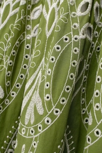 Detailed view of green cotton fabric featuring intricate white embroidery and openwork details