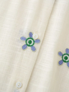 Gros plan détaillé de la broderie de marguerites et boutons sur chemise en lin