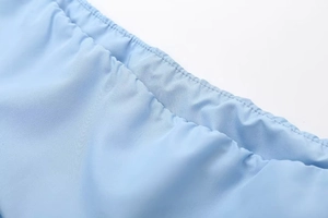 Close-up of light blue polyester fabric with precise double-needle stitching on the hem