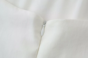 Close-up detail of invisible zipper on white dress with fine woven fabric texture