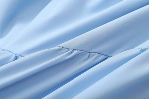 Macro shot of light blue woven fabric featuring pleated stitching and detailed seam work