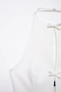 Detail eines weißen Neckholder-Tops mit Metallschnalle und schicken Schleifenakzenten