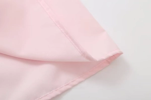Close-up detail of smooth light pink fabric texture and fine stitching on the garment hem
