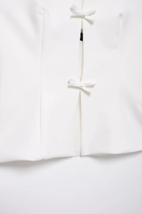 Detail eines weißen Neckholder-Tops mit zarten Schleifenverschlüssen und feiner Textur