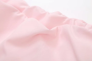 Close-up of light pink woven fabric detailing smooth texture and subtle pleated design