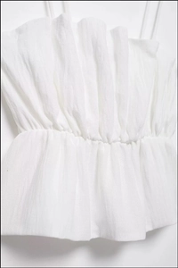 Detailed texture of white elastic smocked camisole with ruffled hem and thin straps