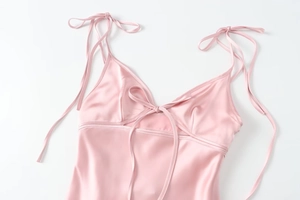 Close-up of pink satin dress featuring delicate bow shoulder straps and silky texture