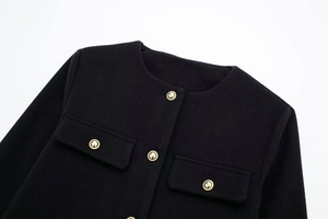 Detail der schwarzen Tweed-Jacke mit goldenen Relief-Knöpfen und symmetrischen Pattentaschen