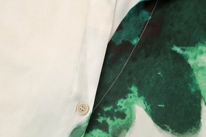 Close-up of green watercolor print fabric with a cream resin button and fine stitching
