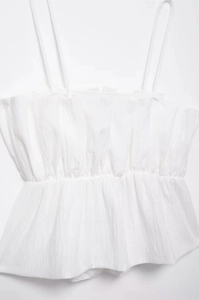 Detail of white peplum camisole showing pleated chest and textured woven fabric
