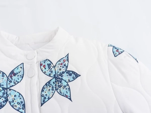 Detail view of wave-quilted jacket collar with buttons and blue floral patch