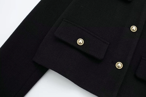 Detailaufnahme von schwarzem Tweed-Stoff mit goldgeprägten Knöpfen und Taschenklappe