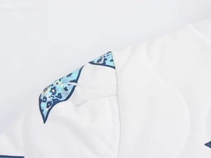 Macro shot of quilted fabric with floral patchwork and stitching details on a white jacket