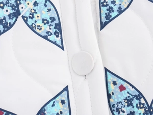 Detail of white quilted jacket with blue floral print and matching fabric-covered button