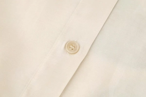 Close-up detail of smooth cream shirt fabric with premium stitching and a four-hole button