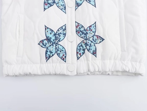 Detail of white quilted vest featuring blue floral butterfly patches and fabric buttons