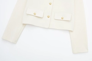 Detailansicht der cremefarbenen Tweedjacke mit goldenen Reliefknöpfen und Taschenstruktur