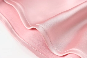 Detail shot of pink satin dress fabric showing smooth texture and precision stitching