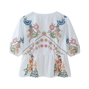 Detail of colorful floral embroidery on white V-neck cotton top with ruffled hemline