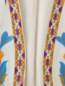 Détail macro de broderie florale colorée bohème sur tissu de gilet blanc