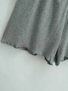 Detail of grey wide-leg shorts featuring elastic ribbed fabric and wavy ruffled hemline
