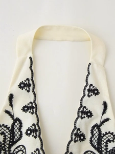 Dettaglio del top bianco con scollo all'americana, ricamo floreale nero e paillette
