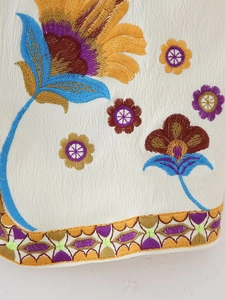 Broderie florale complexe avec tournesols et bordure géométrique colorée sur tissu blanc