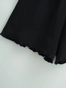 Close-up detail of black ribbed knit fabric featuring decorative lettuce edge stitching