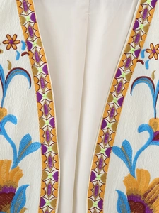 Détail de la broderie florale colorée sur le gilet en similicuir blanc cassé de qualité