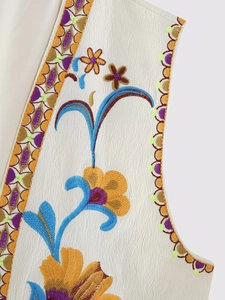 Gros plan de la broderie florale sur un gilet crème avec texture détaillée