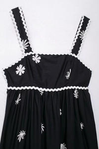 Détail d'une robe midi noire à imprimé marguerites avec des finitions croquet blanc