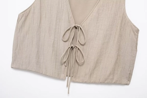 Close-up of beige textured cropped vest featuring two delicate ribbon ties and a V-neckline