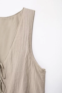 Macro detail of beige textured fabric featuring deep V-neck and drawstring tie accent