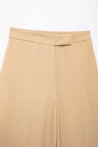 Detail of high-waist khaki wide-leg trousers showing hidden button closure and fabric texture