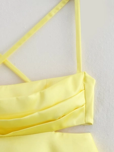 Detail of yellow satin dress featuring cross-tie straps and refined pleated chest craftsmanship