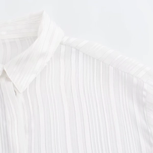 Close-up of white striped shirt fabric with subtle metallic texture and lapel details