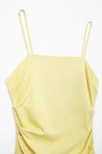 Detail of light yellow summer dress showing thin straps and side ruched texture details
