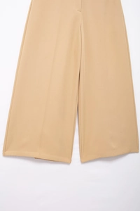 Detail of khaki wide-leg trousers featuring a sharp central crease and fluid fabric texture