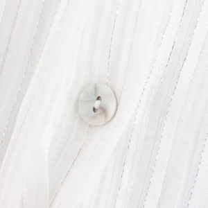 Close-up of white striped fabric with silver metallic threads and marble-textured button