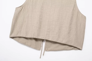 Detail showing the vertical pleated texture and split hem of the beige sleeveless top