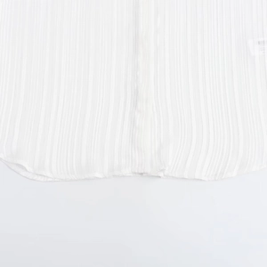 Detail view of the pleated white shirt featuring a curved hem and soft chiffon texture