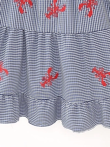 Detail of blue and white gingham fabric with red lobster embroidery and ruffled hemline