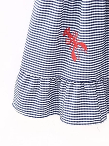 Detail view of blue vichy check dress featuring red lobster embroidery and ruffle hem