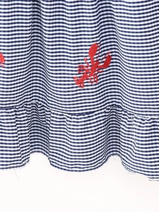 Detail of red lobster embroidery on blue gingham fabric with ruffled hem design