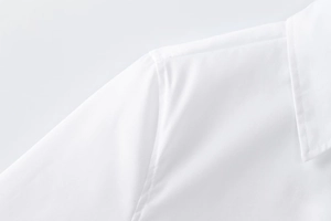 Detailed close-up of white long-sleeved shirt shoulder stitching and collar texture