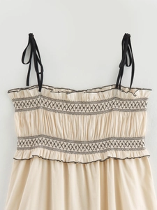 Detail of smocked beige midi dress with black contrast embroidery and adjustable straps