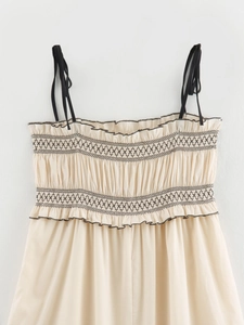 Detailed view of beige midi dress with black smocking, embroidery and ruffle edges