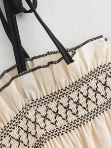 Detailed view of cream-colored fabric with black smocked embroidery and ruffled edges