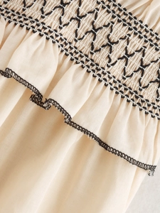 Detailed view of beige midi dress with black smocked embroidery and ruffled edge texture